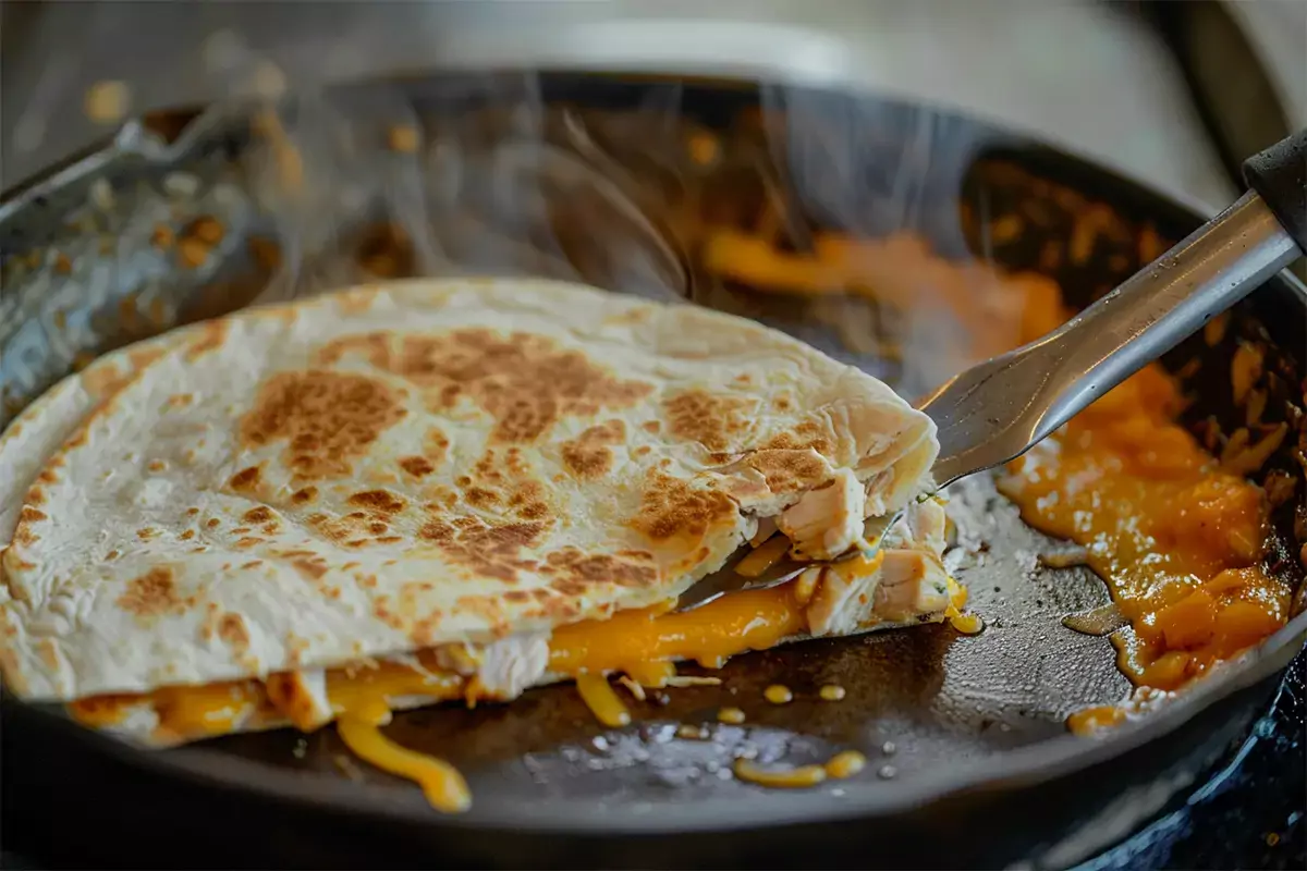 Assembled chicken quesadilla on a skillet with cheese melting out and a spatula pressing it down, ready to cook